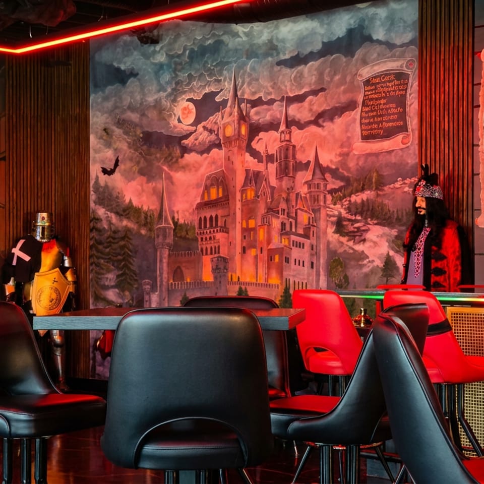 Gothic-themed restaurant interior with red neon lighting, black seating, bar counter, medieval castle mural, and Dracula-themed decor.