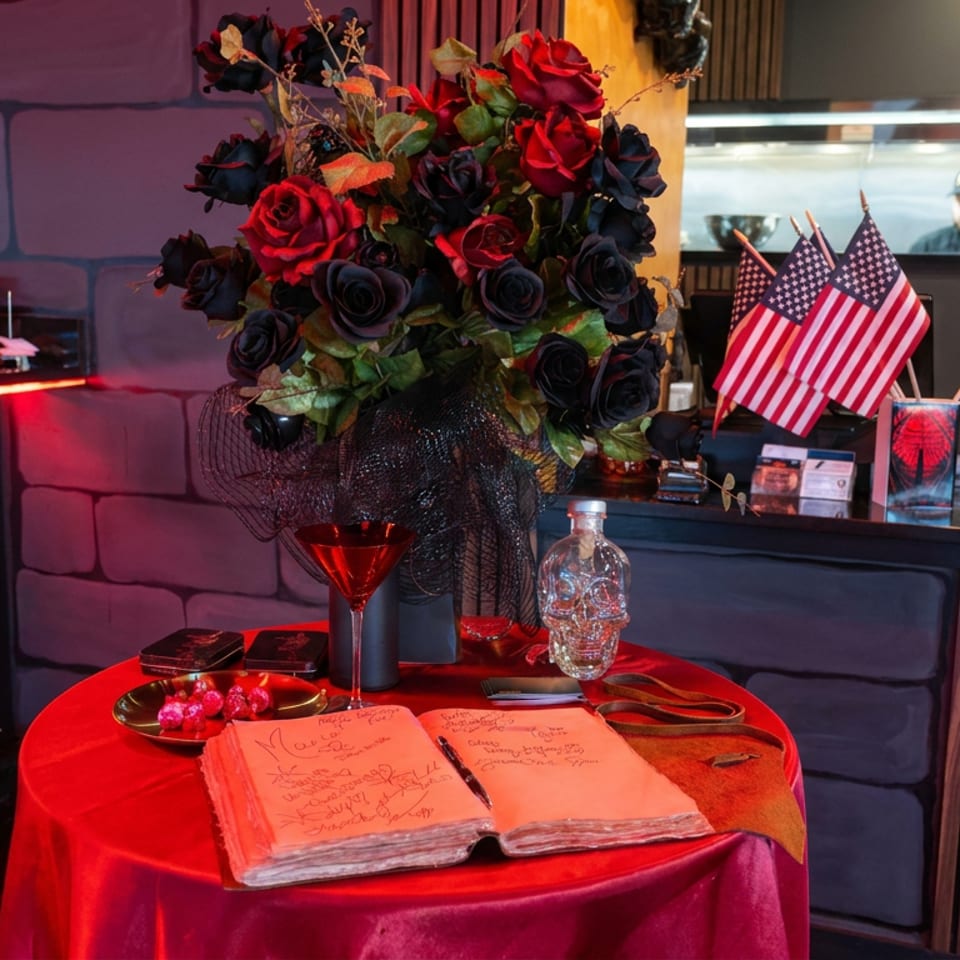 Restaurant table decorated with red and black roses, American flags, a wine glass, candies, and an open guestbook.